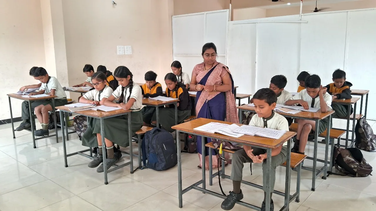 Primary cadets in uniform seated at wooden desks reading and writing while a teacher supervises the classroom at Cardinal Warriors.