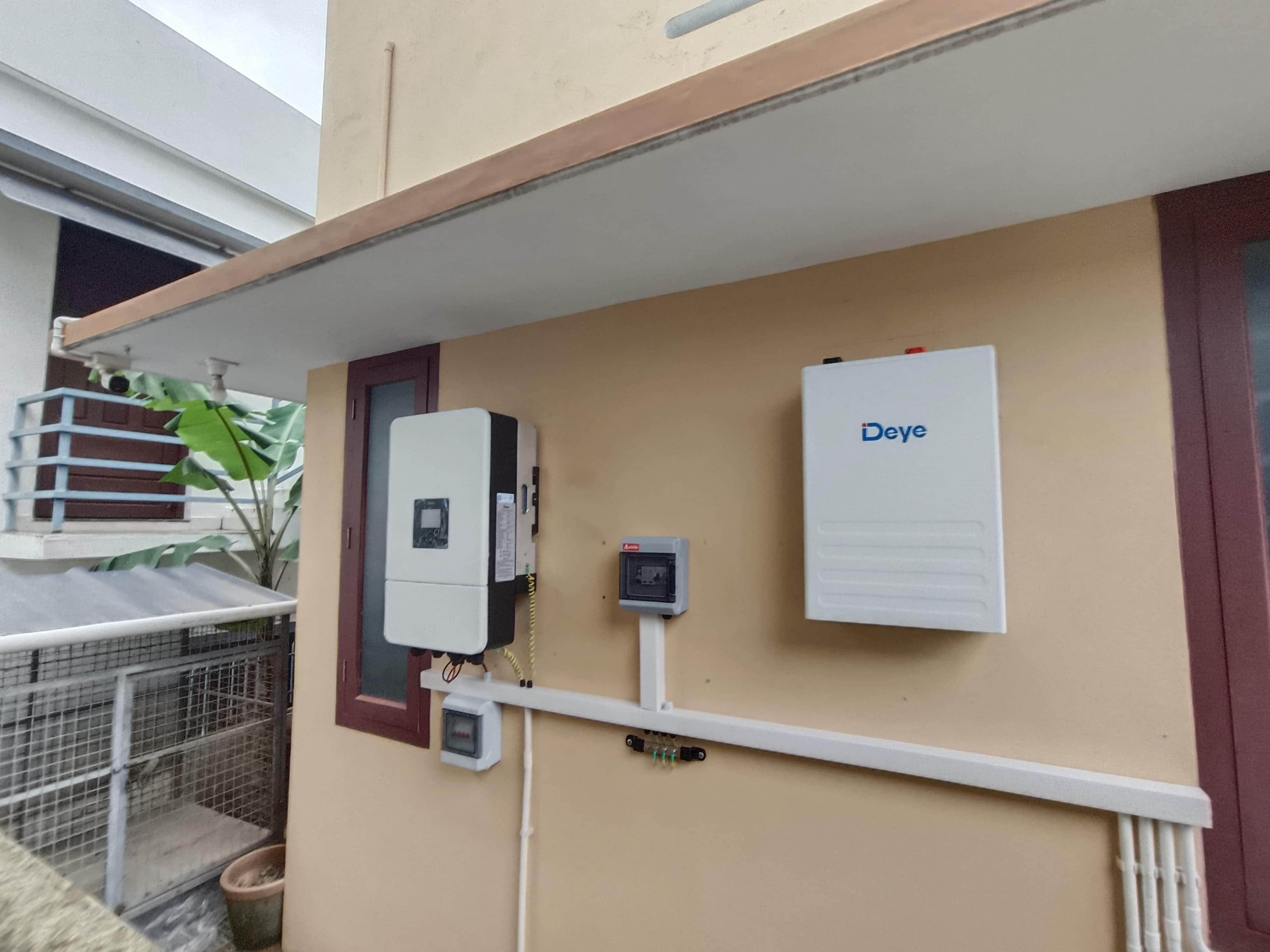 Close-up of a hybrid solar inverter and battery setup inside a Kerala home utility room. photorealistic close-up photo of a hybrid solar inverter mounted on a wall next to a lithium battery pack in a clean home utility room in Kerala