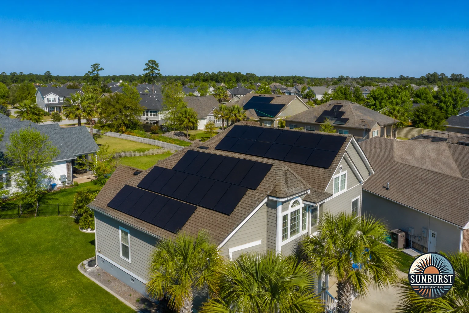 Aerial or elevated view of a South Carolina neighborhood with several homes featuring rooftop solar panels. Photorealistic photo: an elevated view of a South Carolina suburban neighborhood at midday with several rooftops featuring black
