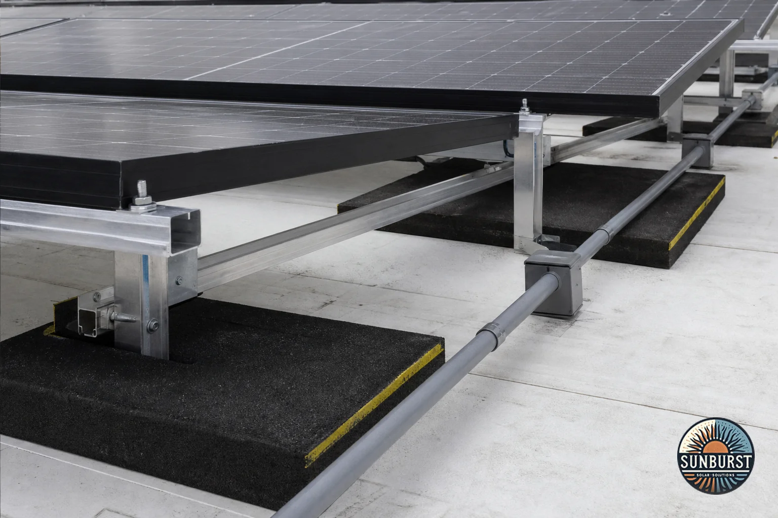 Close-up of solar racking and mounting hardware on a commercial flat roof. Photorealistic close-up photograph of solar panel racking and ballasted mounting hardware installed on a flat commercial TPO roof membrane, showing aluminum rails