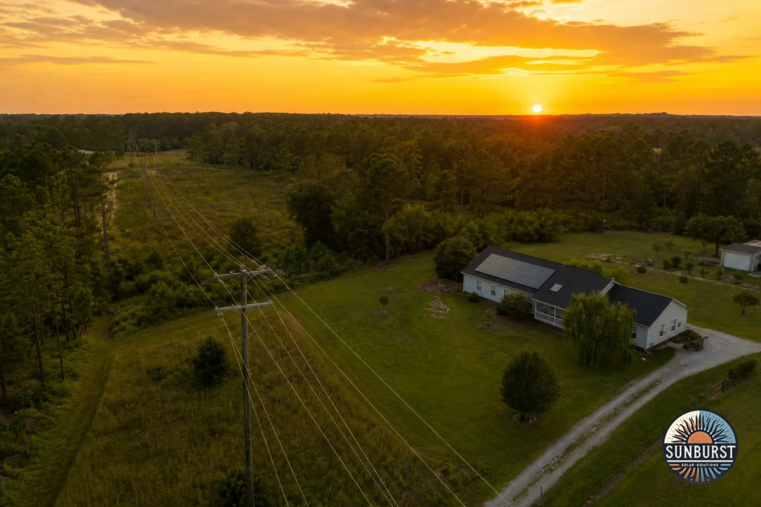 Map-like aerial view of South Carolina landscape showing utility infrastructure. Photorealistic aerial drone photograph over a South Carolina landscape showing power distribution lines and utility poles running past a rural home with solar
