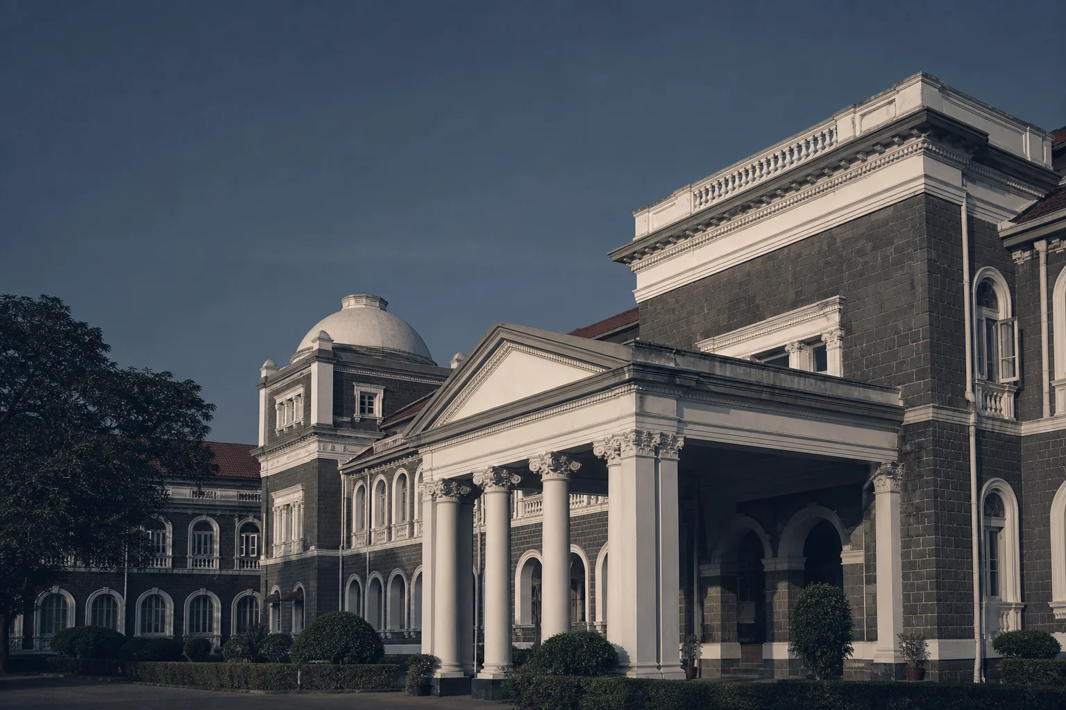 photorealistic photograph of an Indian courthouse building exterior with classic colonial architecture, photographed from a low angle under a clear sky in soft late-afternoon light, desaturated color grade leaning toward dark blue and grey