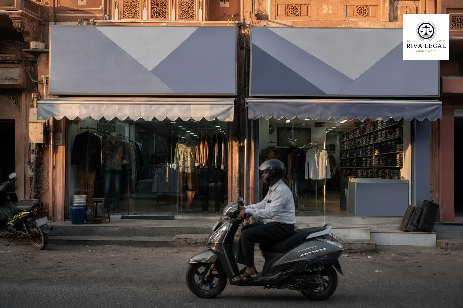 Photorealistic photo of a small Indian retail storefront street scene in a city like Jaipur, two adjacent shop signs with similar generic branding styles but no readable text, warm afternoon light with a subtle cool blue-grey color grade