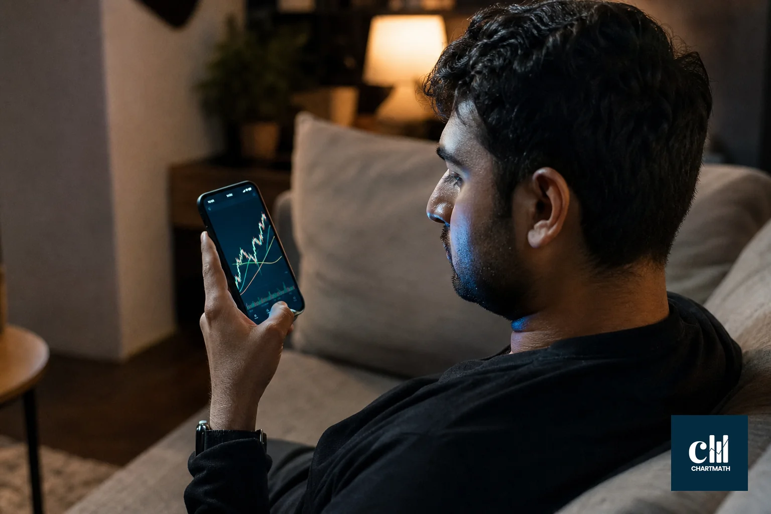 An Indian swing trader looking at his phone showing a stock chart with a moving average crossover, uncertain expression, evening setting. photorealistic photo of a young Indian man in his early 30s sitting on a home sofa in the evening