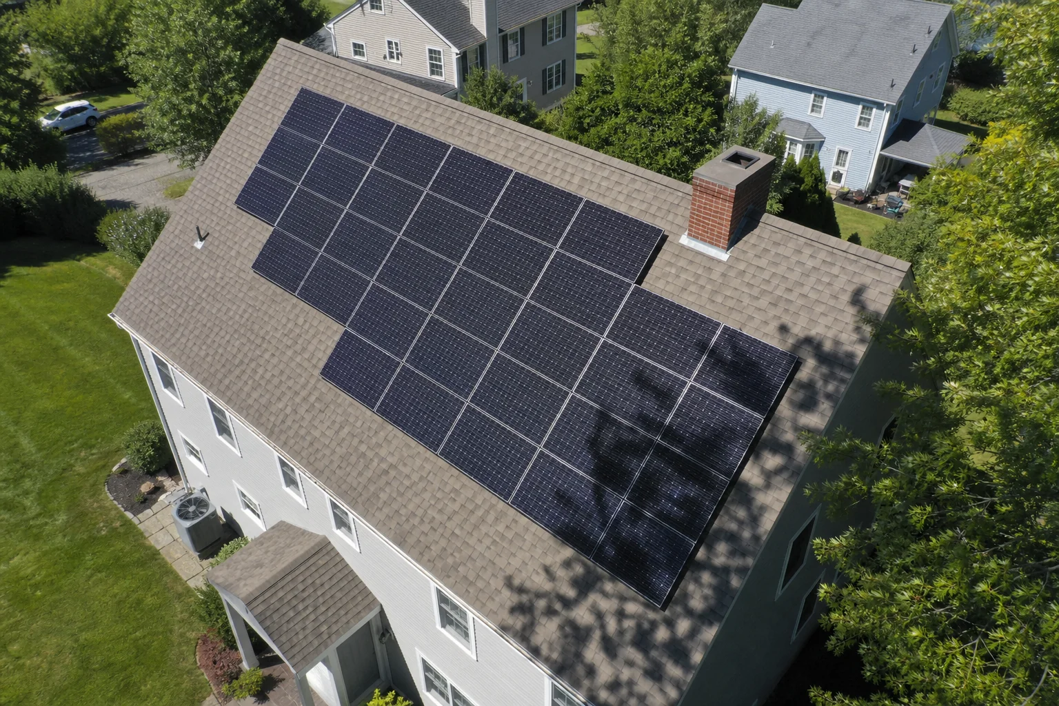 Photorealistic aerial drone shot of a residential roof showing solar panel layout with some shaded areas from trees. Photorealistic aerial drone photograph of a suburban New England home rooftop with solar panels installed on the