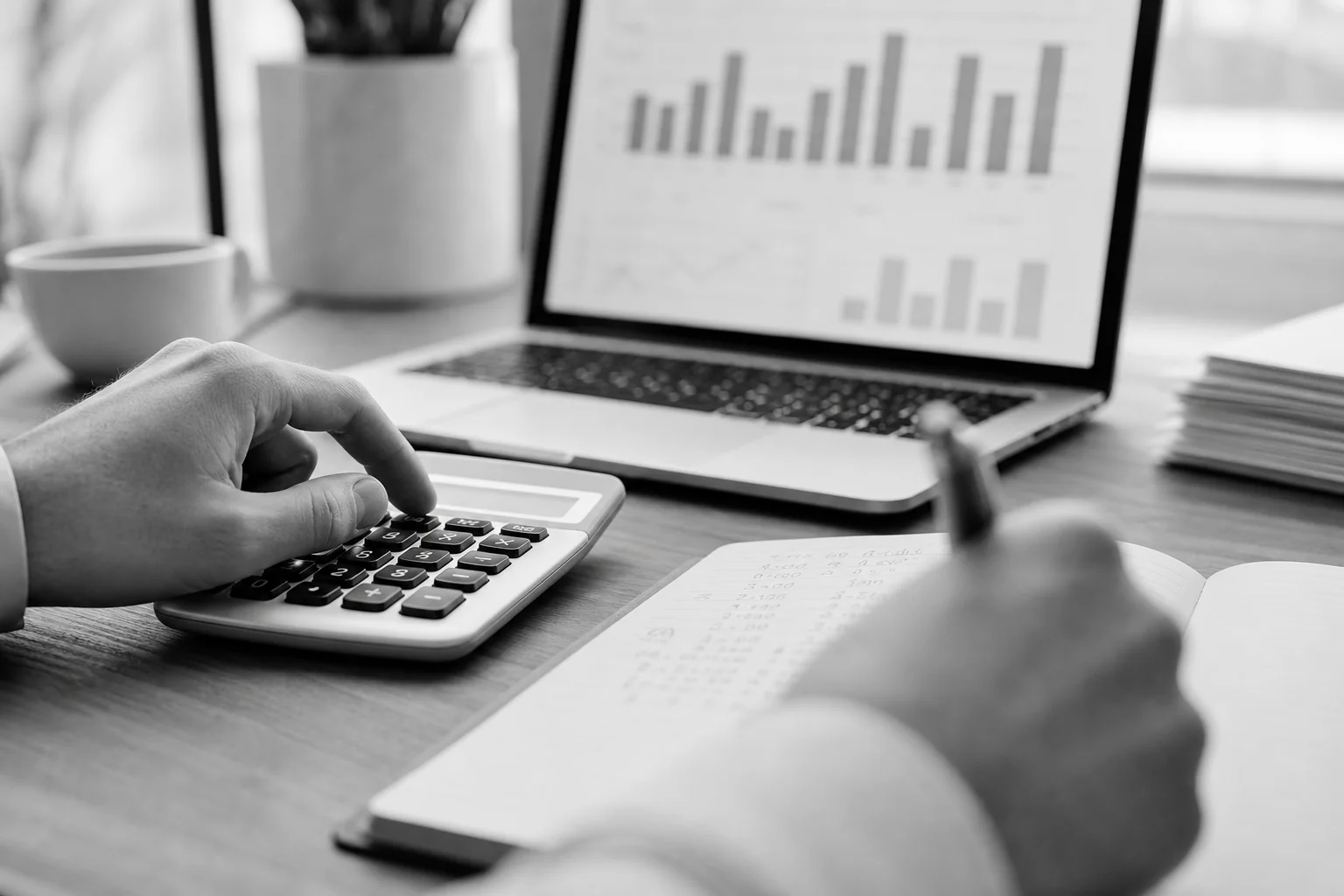 Close-up of hands calculating costs with a calculator, notebook, and laptop showing charts. Photorealistic close-up photo of hands working at a desk with a calculator, an open notebook with handwritten numbers, and a laptop screen showing