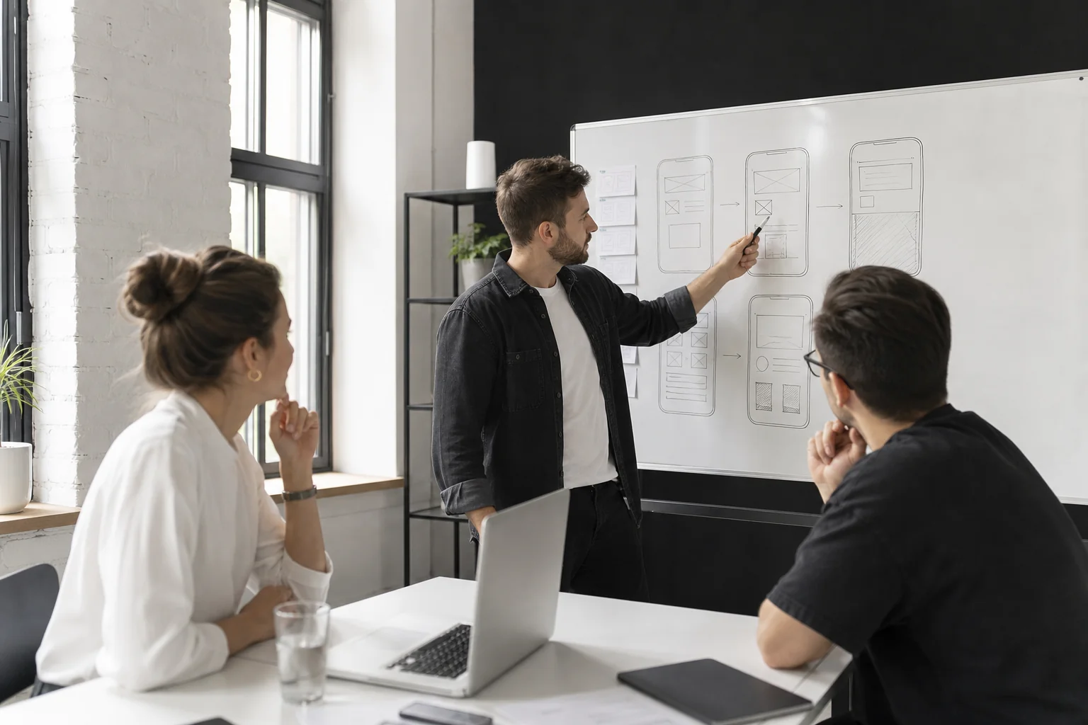 Small development team reviewing a mobile app wireframe on a whiteboard during a cost and scope planning session