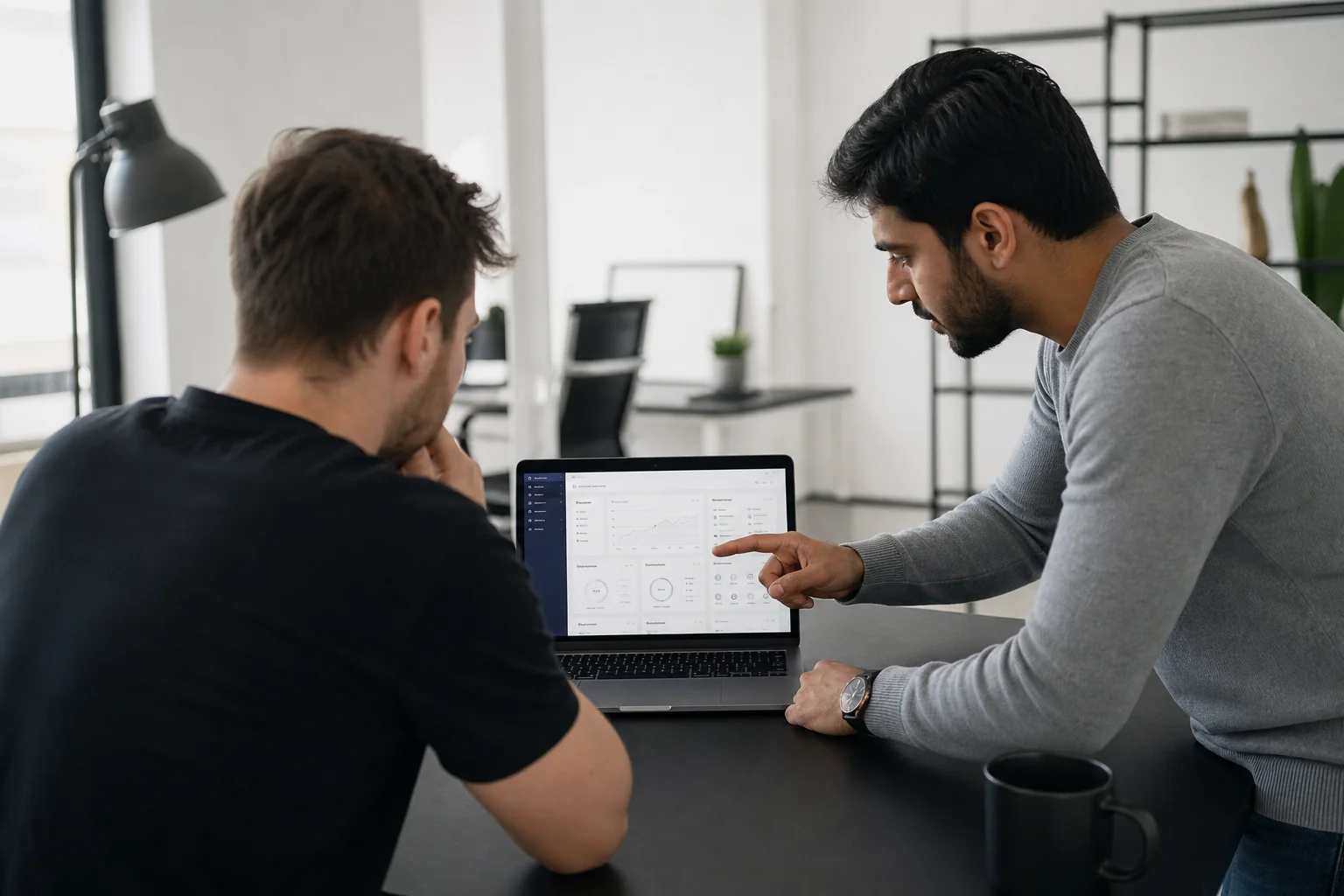Developer team collaborating on a React/Next.js SaaS project. Photorealistic photo: two developers collaborating around a laptop showing a Next.js SaaS dashboard interface, modern startup office, black and white minimalist decor, natural