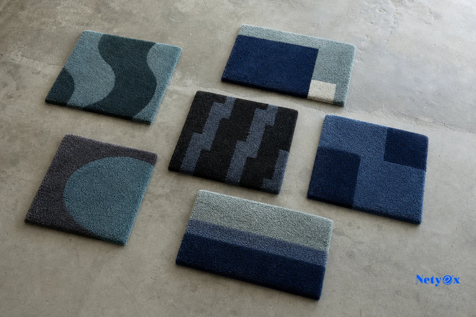 Custom rug design samples laid out for buyer approval. Photorealistic photo of several small hand tufted wool rug samples in different geometric patterns and colorways laid flat on a concrete studio floor, viewed from above, natural