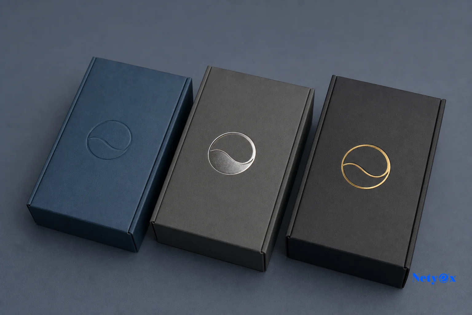 Photorealistic photo of three custom packaging prototype boxes with different logo embossing and foil-stamp finishes arranged on a clean studio table for approval comparison, soft studio lighting, muted brand color palette of blue and slate