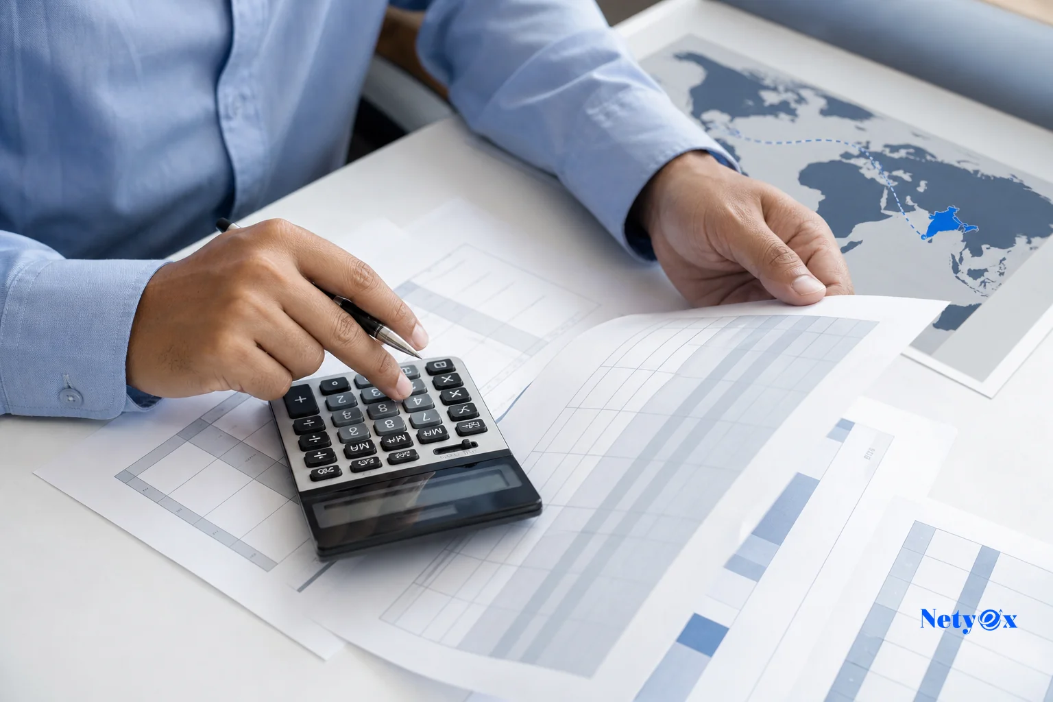 Close-up of hands calculating shipping and cost figures with a calculator, invoice papers, and a world map showing trade routes from India. photorealistic photo of hands using a calculator over printed invoices and a shipping cost worksheet